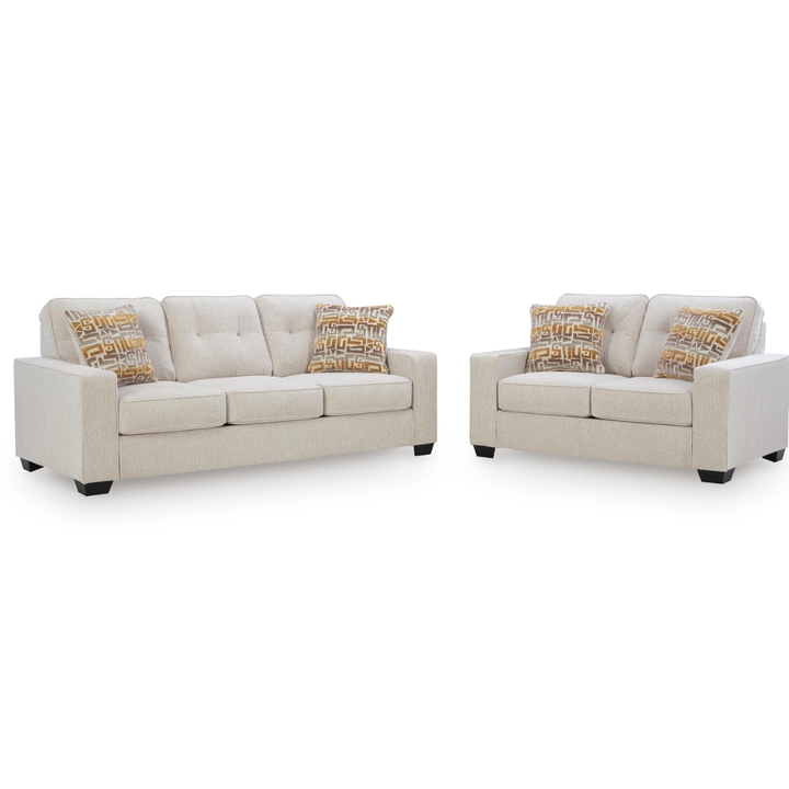 A light beige upholstered living room set consisting of a three-seat sofa and a two-seat loveseat, both with tufted back cushions and two patterned accent pillows in beige, brown, and gold, shown on a plain white background.